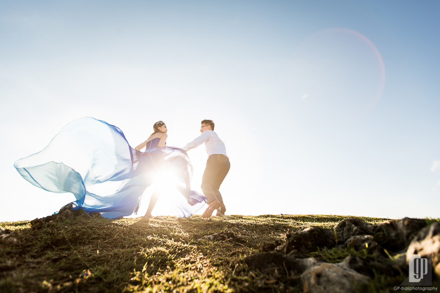 prewedding in tegal wangi beach bali smile happy sunset with love couple majestic beautiful cave and cliff waves blue gown and shirt green grass